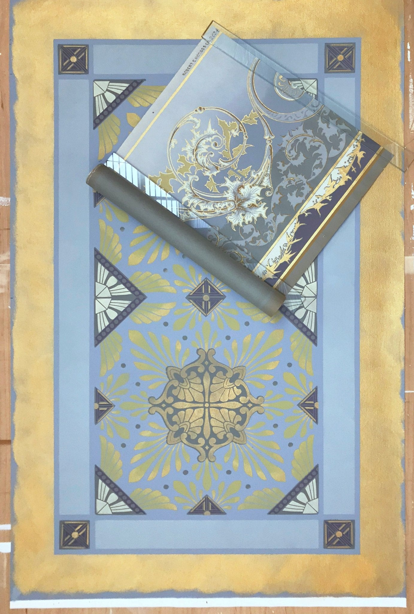 This image shows this floorcloth, based on a Christopher Dresser pattern, with it's palette inspiration, a piece of wallpaper, c. 1880, lying on top.