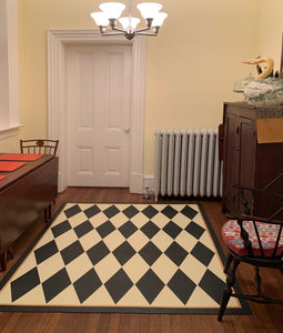 In-situ image of this 5'3" x 6' harlequin patterned floorcloth in a soft yellow-white and charcoal colorway.
