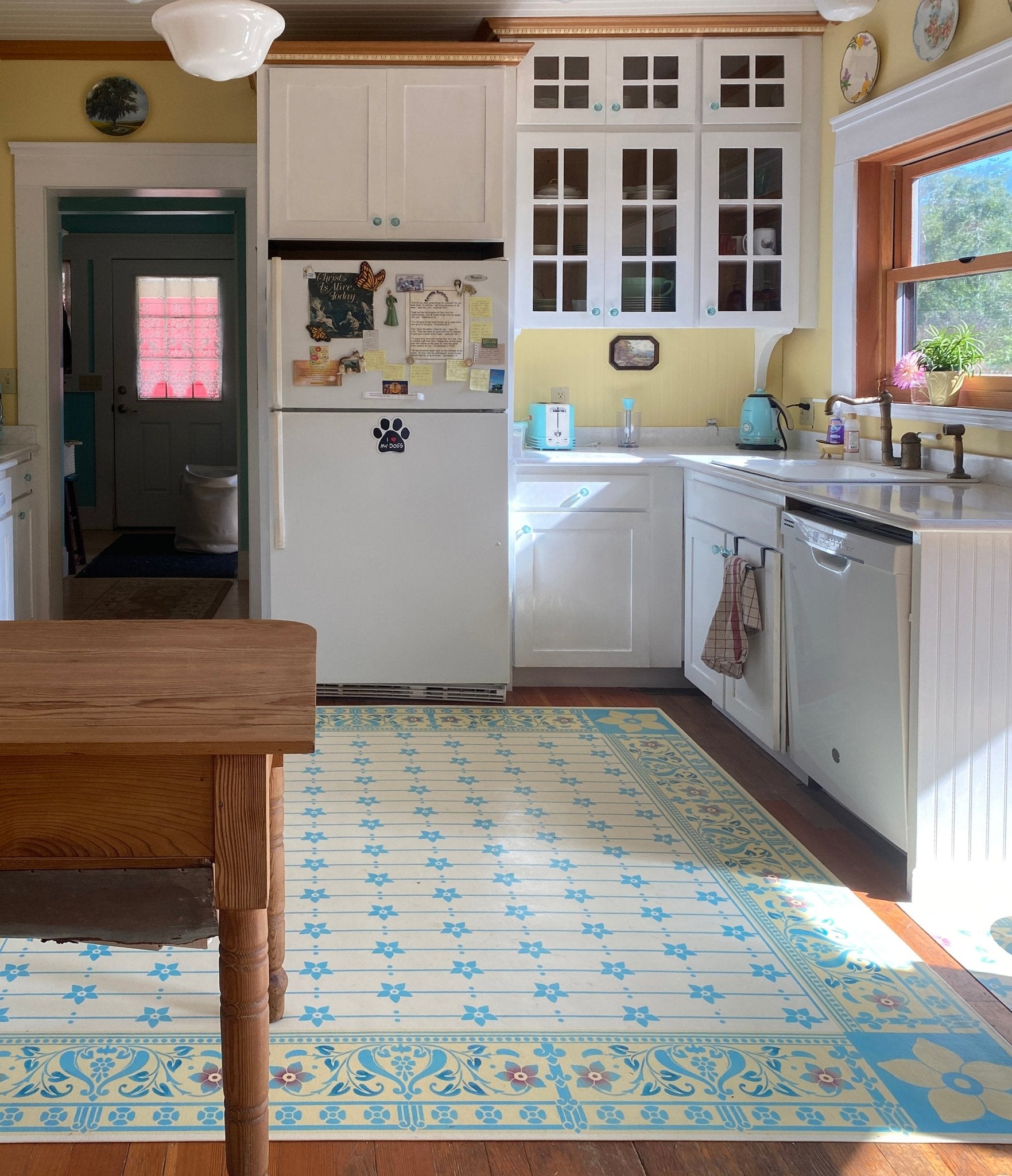 An in-situ photo of this floorcloth in a lovely farmhouse kitchen with Nostalgia appliances in blue, with a matching blue in the floorcloth motifs.